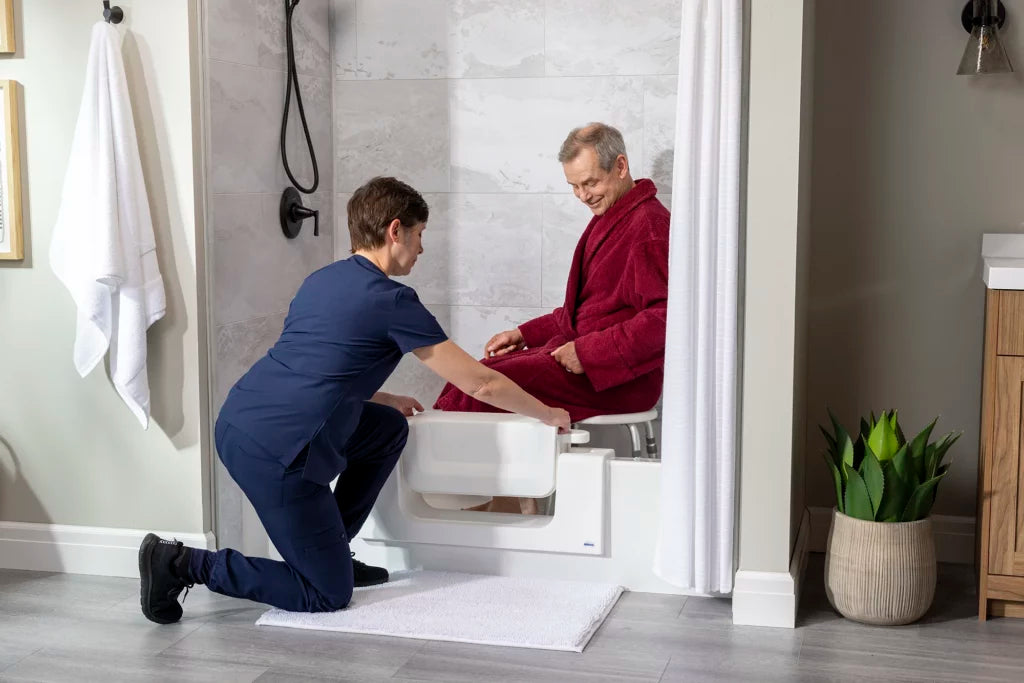 Caregiver helping a senior step into a bathtub through a CleanCut Convertible cutout